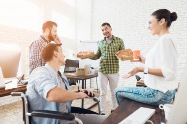 Ofis çalışanları ve adam tekerlekli sandalyede pizza yiyorlar. Onlar bir aydınlık ve modern ofis iş.