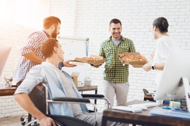 Ofis çalışanları ve adam tekerlekli sandalyede pizza yiyorlar. Onlar bir aydınlık ve modern ofis iş.