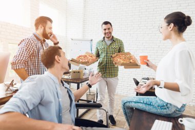 Ofis çalışanları ve adam tekerlekli sandalyede pizza yiyorlar. Onlar bir aydınlık ve modern ofis iş.