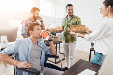 Ofis çalışanları ve adam tekerlekli sandalyede pizza yiyorlar. Onlar bir aydınlık ve modern ofis iş.