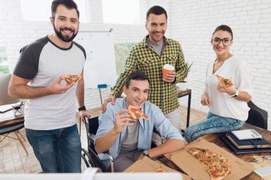 Ofis çalışanları ve adam tekerlekli sandalyede pizza yiyorlar. Onlar bir aydınlık ve modern ofis iş.