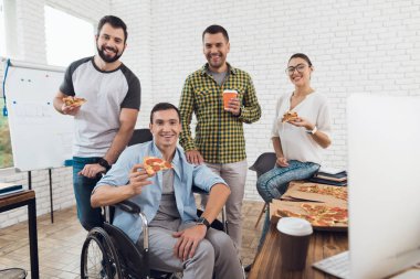 Ofis çalışanları ve adam tekerlekli sandalyede pizza yiyorlar. Onlar bir aydınlık ve modern ofis iş.