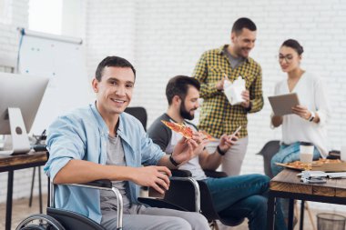 Tekerlekli sandalyede bir adam bir parça pizza tutan kameraya poz veriyor..