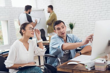 Tekerlekli sandalyede bir adam bir şeyler meslektaşı için bilgisayarda gösteriyor.