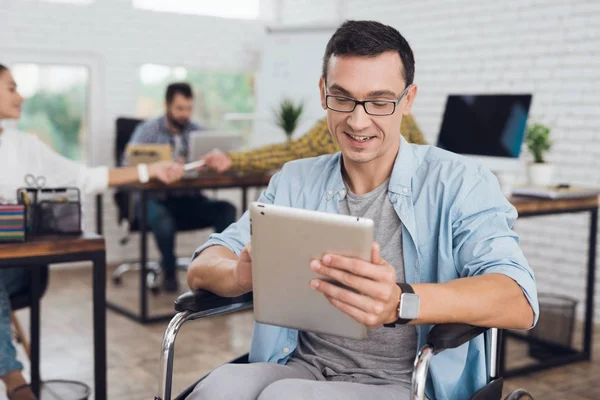 Behinderte im Rollstuhl arbeiten im Büro. In seinen Händen liegt eine Tablette. — Stockfoto