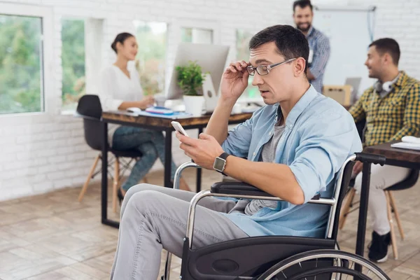 Gehandicapte persoon in de rolstoel werkt op kantoor. Hij praat op smartphone. — Stockfoto