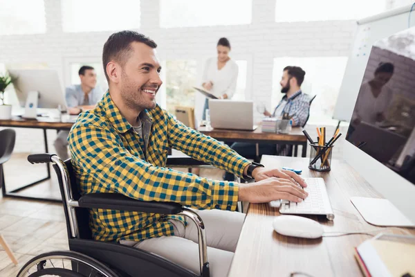 Un hombre en silla de ruedas está trabajando en la computadora en una mesa en una oficina moderna . — Foto de Stock