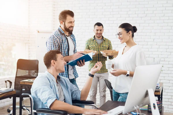 Ofis çalışanları ve adam tekerlekli sandalyede pizza yiyorlar. Onlar bir aydınlık ve modern ofis iş.