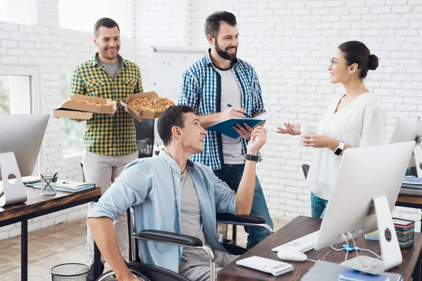 Office workers and man in a wheelchair are eating pizza. They work in a bright and modern office.