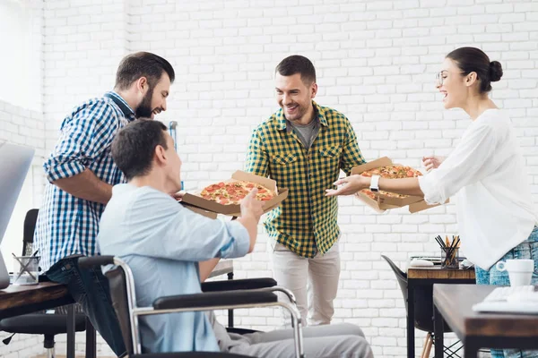Ofis çalışanları ve adam tekerlekli sandalyede pizza yiyorlar. Onlar bir aydınlık ve modern ofis iş.