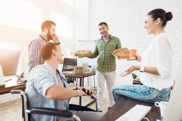 Ofis çalışanları ve adam tekerlekli sandalyede pizza yiyorlar. Onlar bir aydınlık ve modern ofis iş.