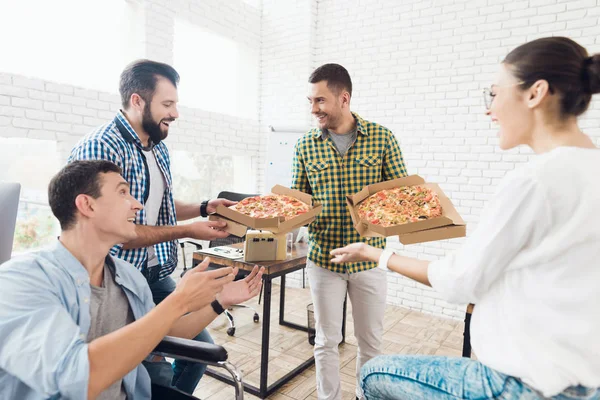Büroangestellte und ein Mann im Rollstuhl essen Pizza. Sie arbeiten in einem hellen und modernen Büro. — Stockfoto