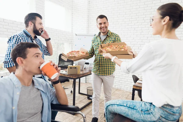 Trabalhadores de escritório e homem em uma cadeira de rodas estão comendo pizza. Eles trabalham em um escritório brilhante e moderno . — Fotografia de Stock