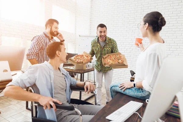 Ofis çalışanları ve adam tekerlekli sandalyede pizza yiyorlar. Onlar bir aydınlık ve modern ofis iş.