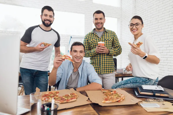 Kontorarbeidere og menn i rullestol spiser pizza. De jobber på et lyst og moderne kontor. . – stockfoto