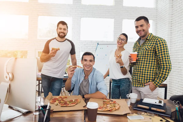 Trabalhadores de escritório e homem em uma cadeira de rodas estão comendo pizza. Eles trabalham em um escritório brilhante e moderno . — Fotografia de Stock