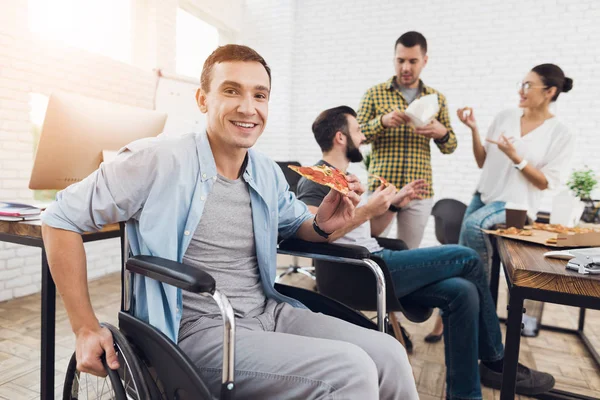 En man i rullstol utgör på kameran håller en bit pizza. — Stockfoto