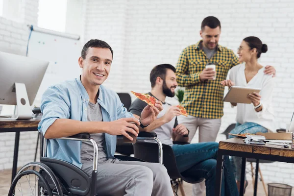 Tekerlekli sandalyede bir adam bir parça pizza tutan kameraya poz veriyor..