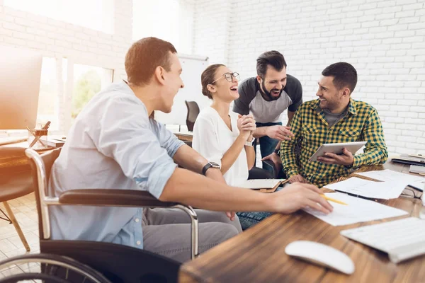 Gli impiegati e una persona sulla sedia a rotelle discutono di questioni di lavoro. Lavorano in un ufficio luminoso . — Foto Stock