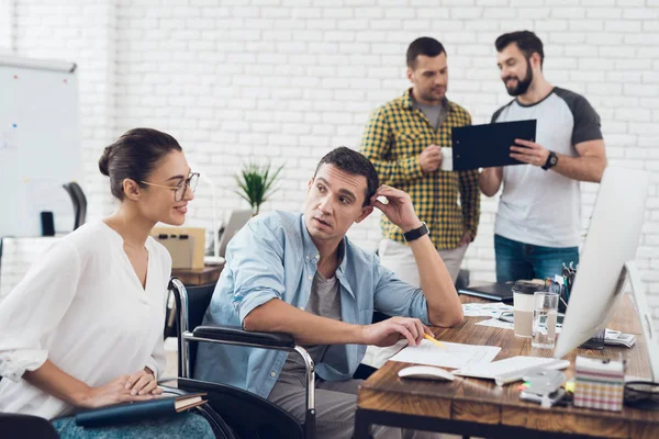 Een man in een rolstoel is het maken van een gesprek met een meisje. Ze werken in een heldere kantoor. — Stockfoto