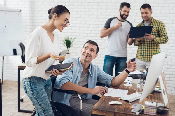 Tekerlekli sandalyede bir adam bir kız ile bir konuşma yapıyor. Onlar parlak bir ofiste çalışıyoruz.