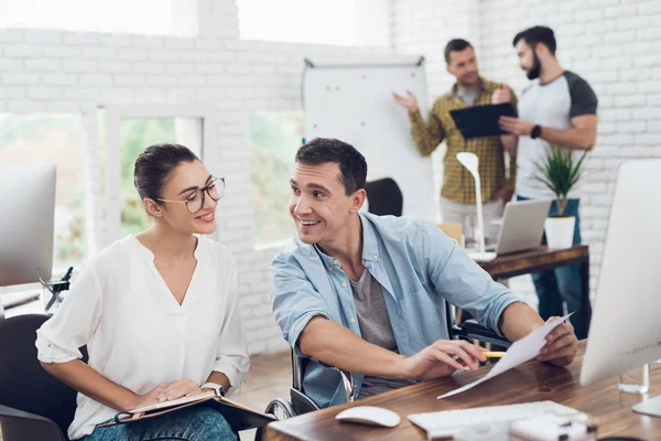 Een man in een rolstoel is het maken van een gesprek met een meisje. Ze werken in een heldere kantoor. — Stockfoto