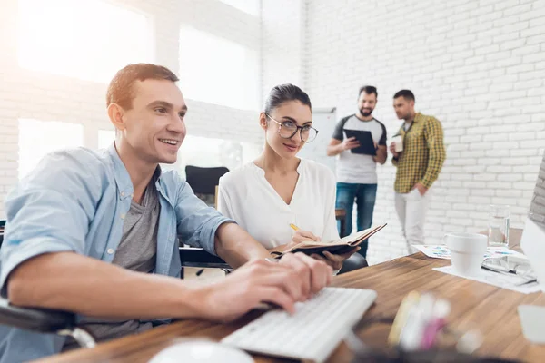 Ein Mann im Rollstuhl zeigt seinem Kollegen etwas am Computer. — Stockfoto