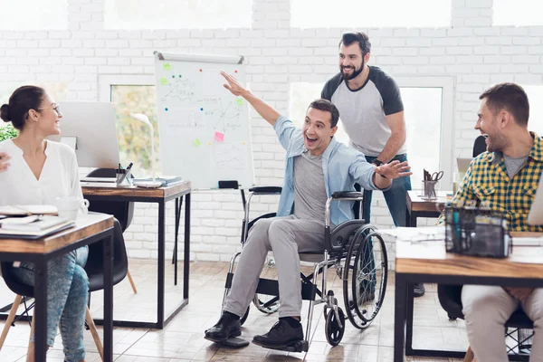 Un collega fa rotolare una persona su una sedia a rotelle in ufficio. Si divertono e ridono . — Foto Stock