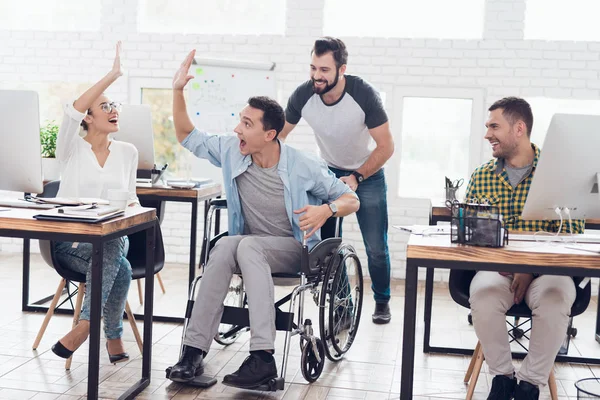 Un collega fa rotolare una persona su una sedia a rotelle in ufficio. Si divertono e ridono . — Foto Stock