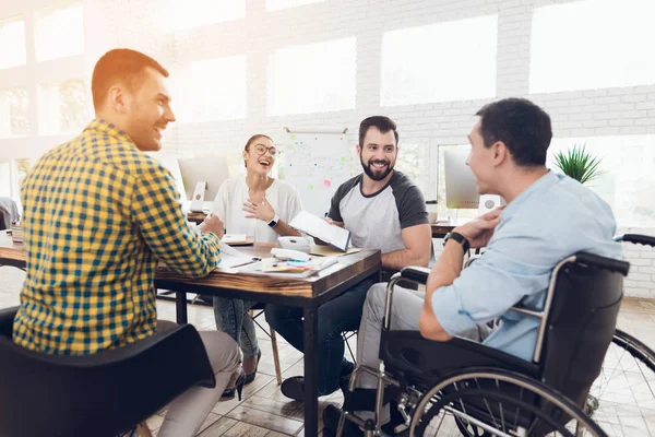Un hombre en silla de ruedas se comunica alegremente con los empleados de la oficina durante una reunión de negocios . —  Fotos de Stock