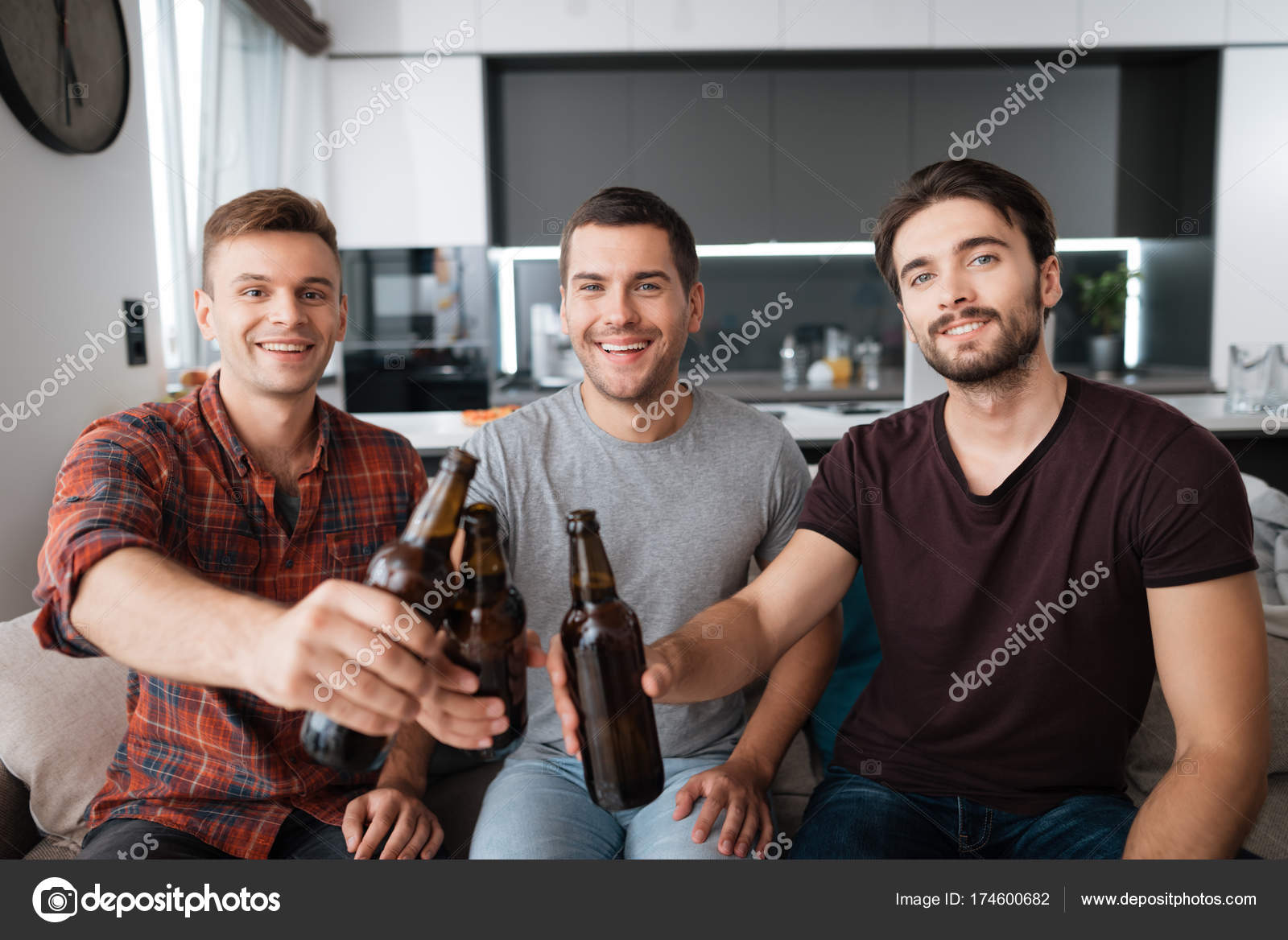 Three men drink beer from dark bottles. They are sitting on the couch