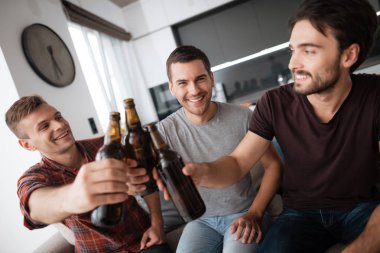 Üç adam karanlık şişe bira içmek. Kanepede oturan ve gülümseyen.