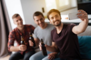 Erkekler kanepede oturan ve bira içmek. Bir adam bir selfie arkadaşlar ve bira ile yapar.