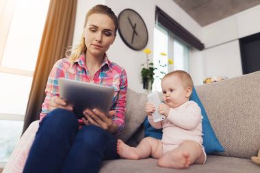 Anne bebek kanepede ve onu oturur yanında oturur. Bir kadın bir şey tablette okur.