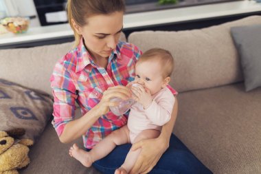 Bir kadın kanepede oturur ve bir çocuk kime o içki için özel bir kavanoz verir kollarında tutar.