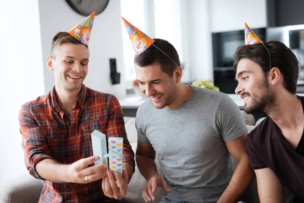 Men in birthday hats are showing to each other presents.