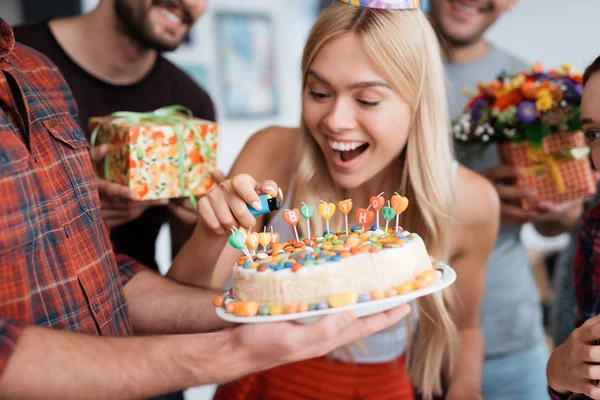 La chica enciende las velas del pastel. Alrededor de ella hay invitados esperando la celebración. . — Foto de Stock