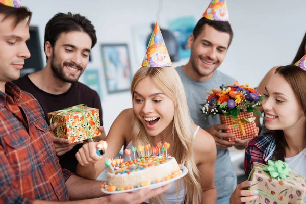 La fille allume les bougies sur le gâteau. Autour d'elle il y a des invités qui attendent la célébration . — Photo