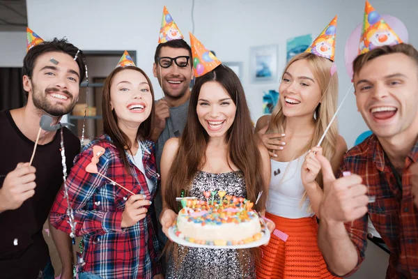 La fille d'anniversaire tient un gâteau avec des bougies. Les filles et les gars sont debout autour d'elle . — Photo