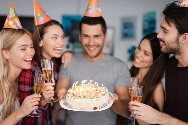 El cumpleaños de un tipo y sus amigos lo felicitan. Los invitados están parados alrededor del cumpleañero. El tipo está sosteniendo un pastel . —  Fotos de Stock