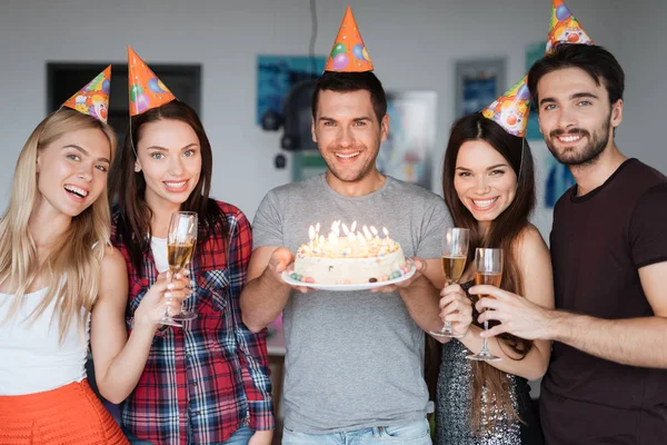 El cumpleaños de un tipo y sus amigos lo felicitan. Los invitados están parados alrededor del cumpleañero. El tipo está sosteniendo un pastel . —  Fotos de Stock