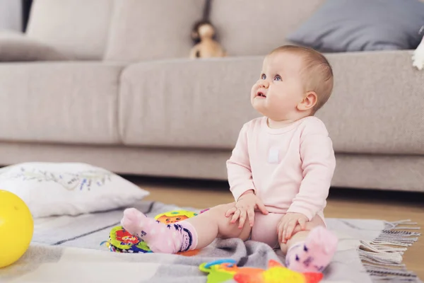 Маленький красивый ребенок сидит на полу и играет с яркими, цветочными игрушками . — стоковое фото