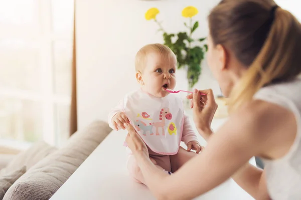 Una mujer está alimentando a un bebé con una cuchara. Un niño se sienta en una mesa en la cocina y come con placer . — Foto de Stock