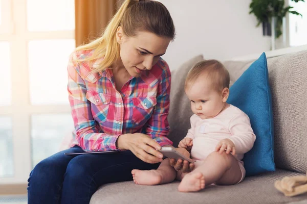 Anne bebek kanepede ve onu oturur yanında oturur. Bir tablet onun kucağına kadındır.