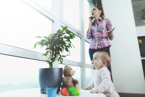 Немовля без нагляду. Поки жінка розмовляє по телефону, її дитина повзе на підлогу і грається . — стокове фото