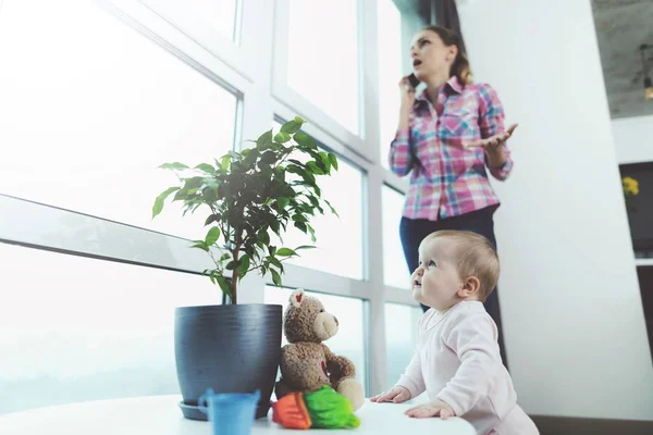 Le bébé est sans surveillance. Pendant que la femme parle au téléphone, son enfant rampant sur le sol et se joue . — Photo