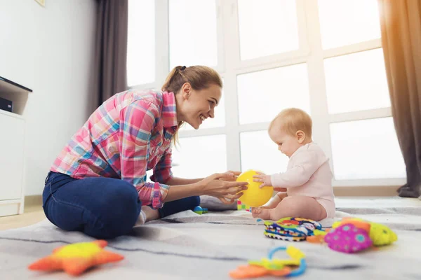 Женщина в розовой рубашке сидит на полу в гостиной и играет со своим маленьким ребенком . — стоковое фото
