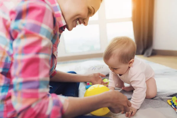 Жінка в рожевій сорочці сидить на підлозі у вітальні і грає зі своєю маленькою дитиною . — стокове фото
