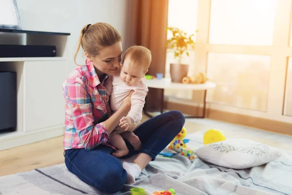 Жінка в рожевій сорочці сидить на підлозі у вітальні і грає зі своєю маленькою дитиною. Дитина дійсно любить грати . — стокове фото