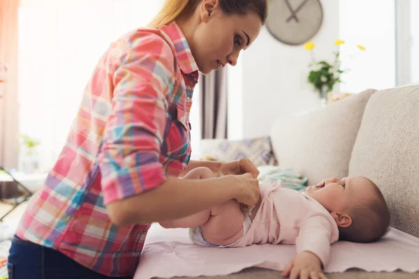 Bir kadın kanepede küçük bir çocuk kundak. Çocuk eğlence güler. Kadın da gülümsüyor.